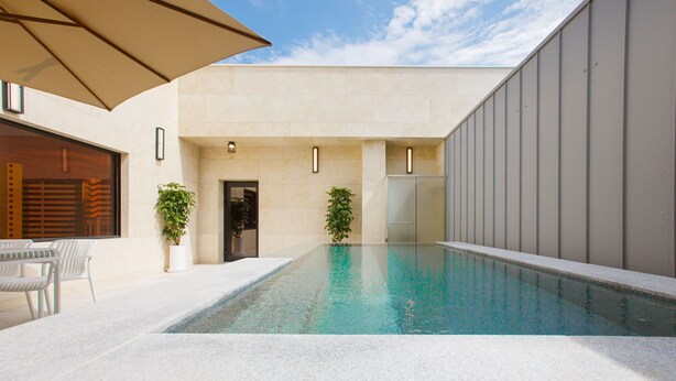A swimming pool with a tiled deck, potted plants, and a covered seating area.