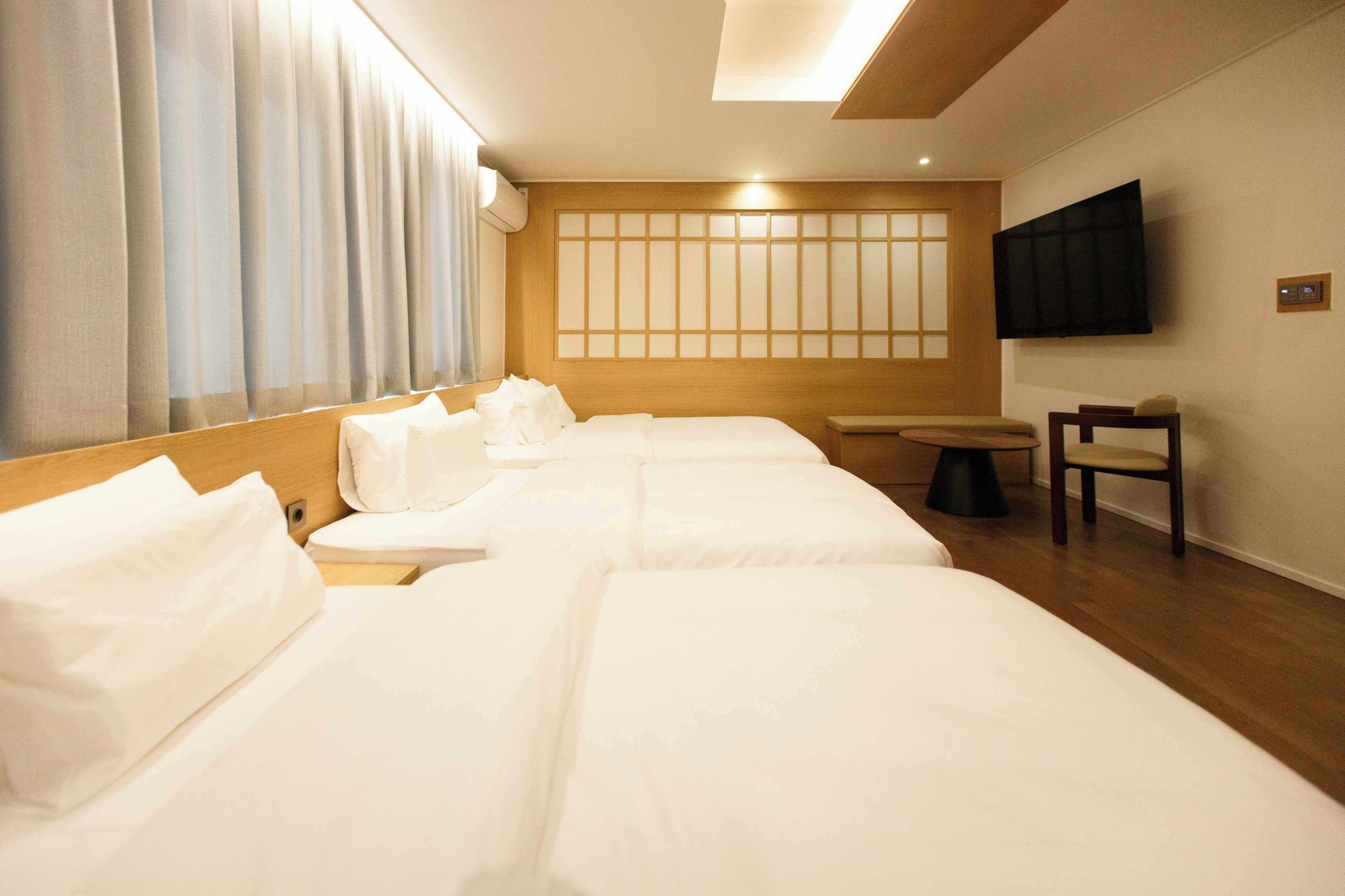 A hotel room with a bed, a TV, a window with curtains, and a wooden headboard.
