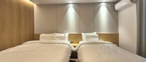 A hotel room with two beds, a skylight, a wall-mounted air conditioner, and a wooden accent wall.