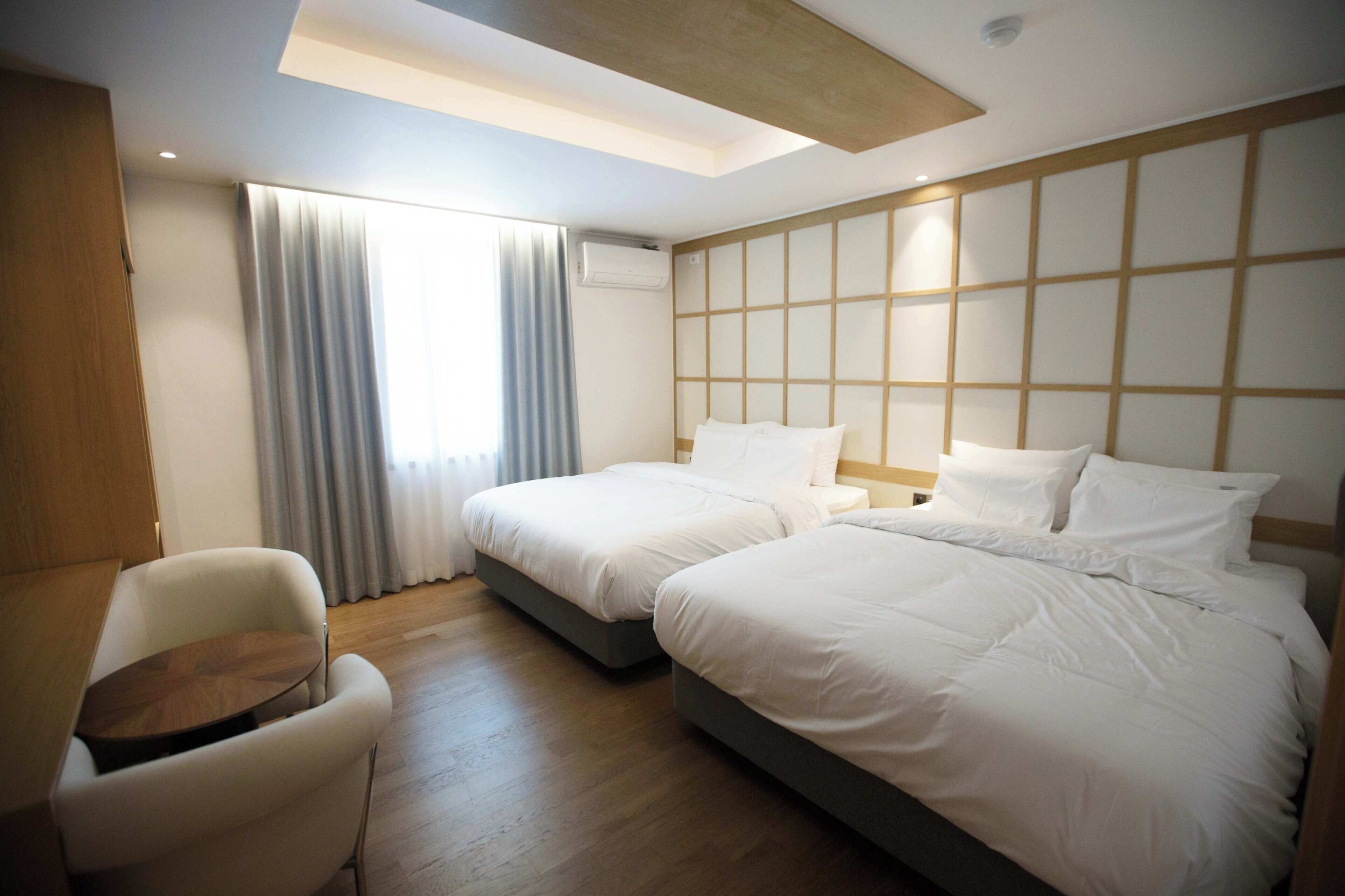 Habitación de hotel con dos camas, un escritorio de madera, una silla y un ventanal con cortinas.