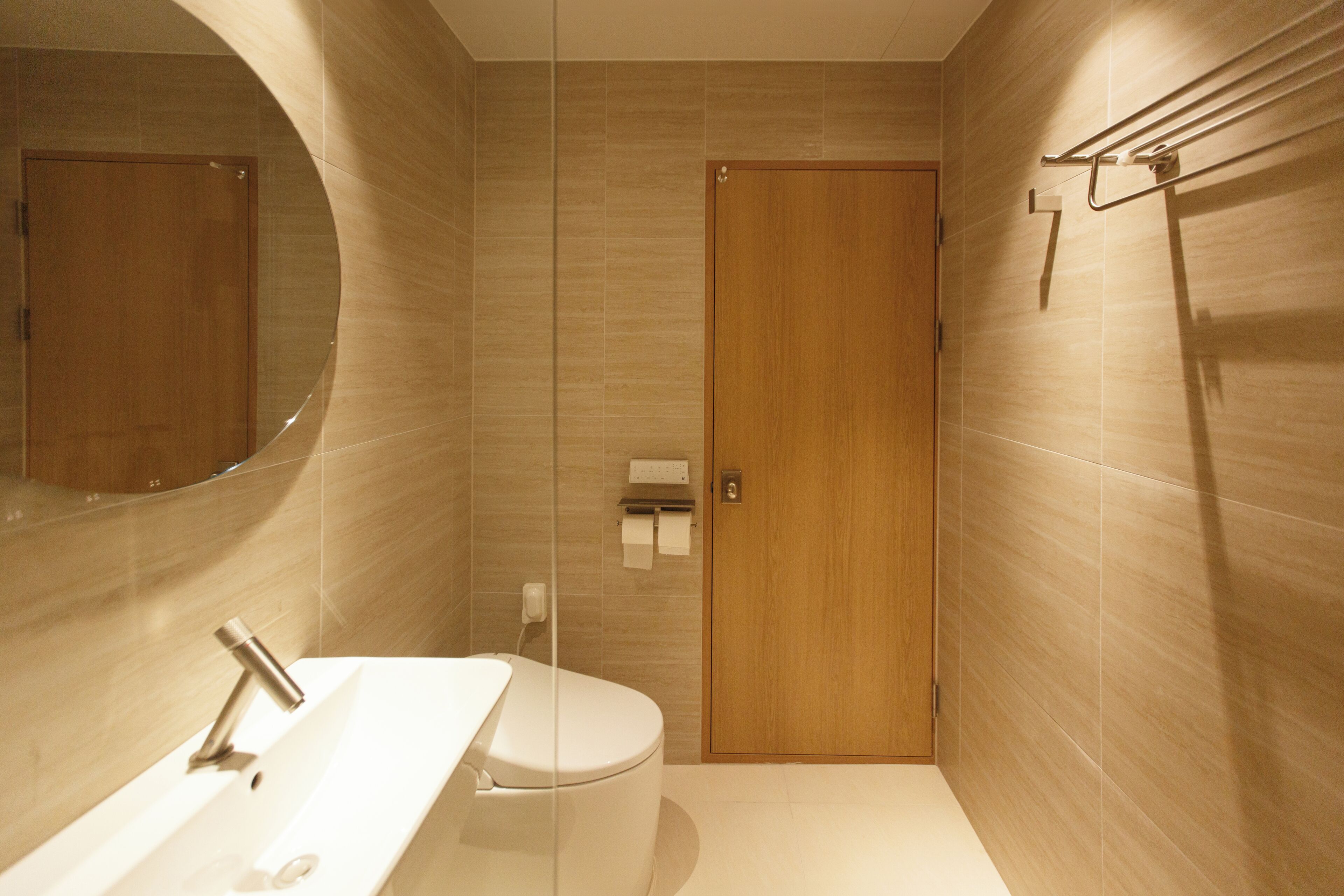 Un baño moderno con puerta de madera, un espejo redondo y un lavamanos blanco.
