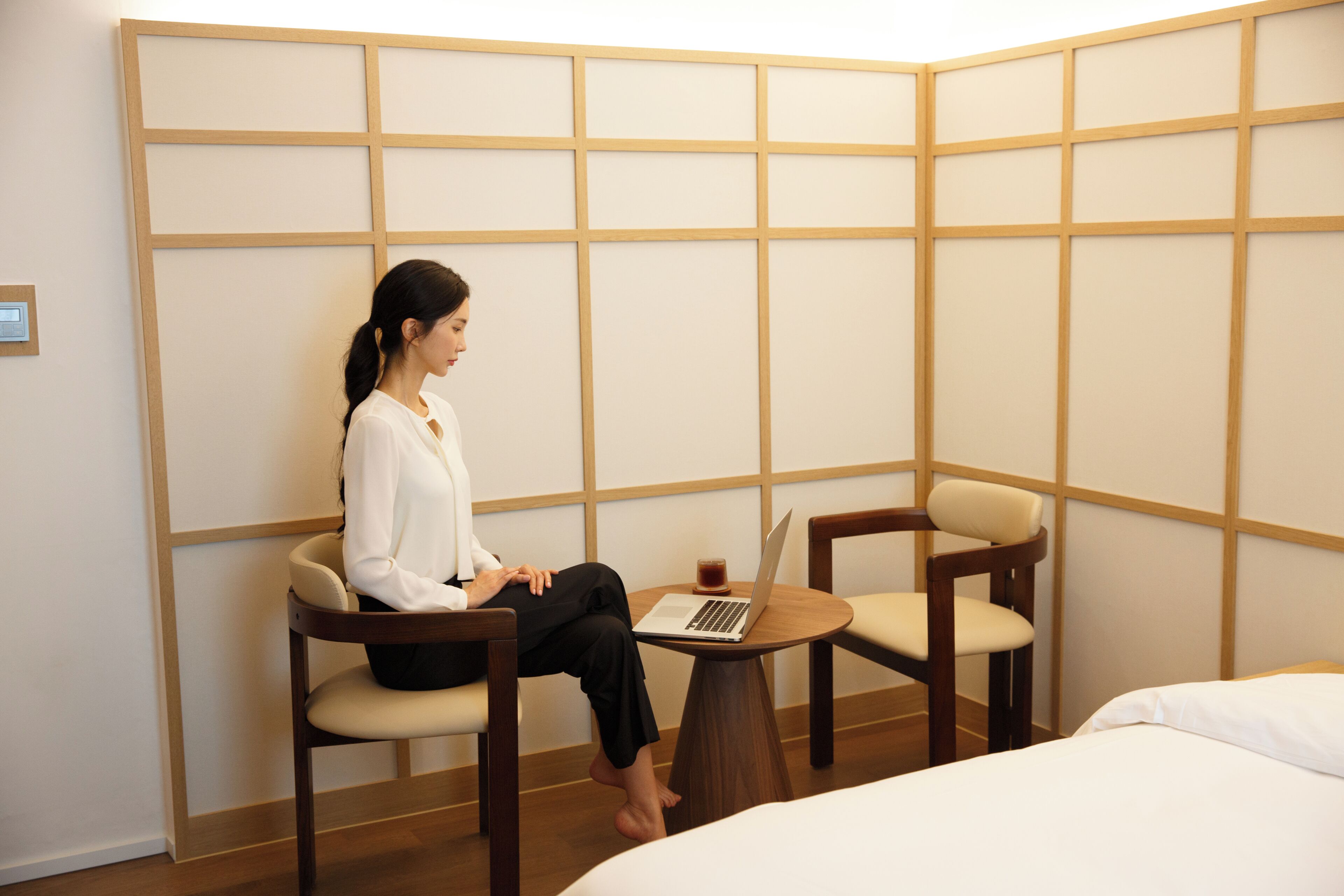 A hotel room with a bed, a desk with a laptop, and two chairs.