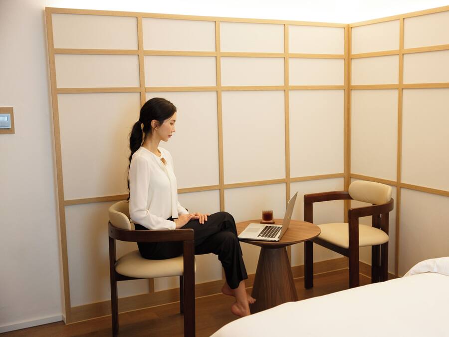 A hotel room with a bed, a desk with a laptop, and two chairs.