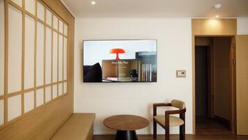 A modern interior with a wooden bench, a round table, a TV mounted on the wall, and a bookshelf.