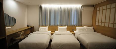 Habitación de hotel con tres camas, un escritorio, una silla, un ventanal con cortinas y un tragaluz.