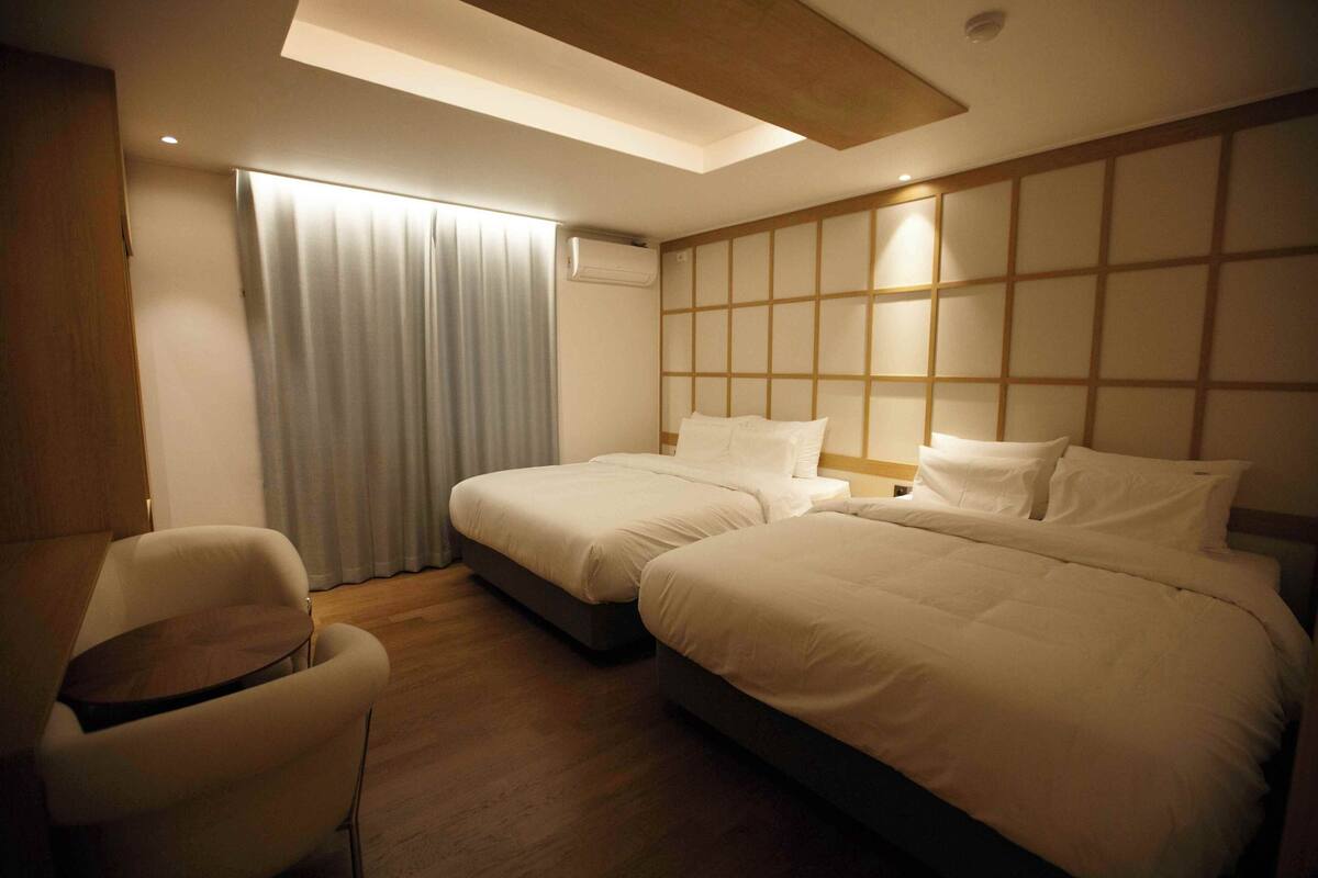 Ein Hotelzimmer mit zwei Betten, einem Sessel und einem Fenster mit Vorhängen.
