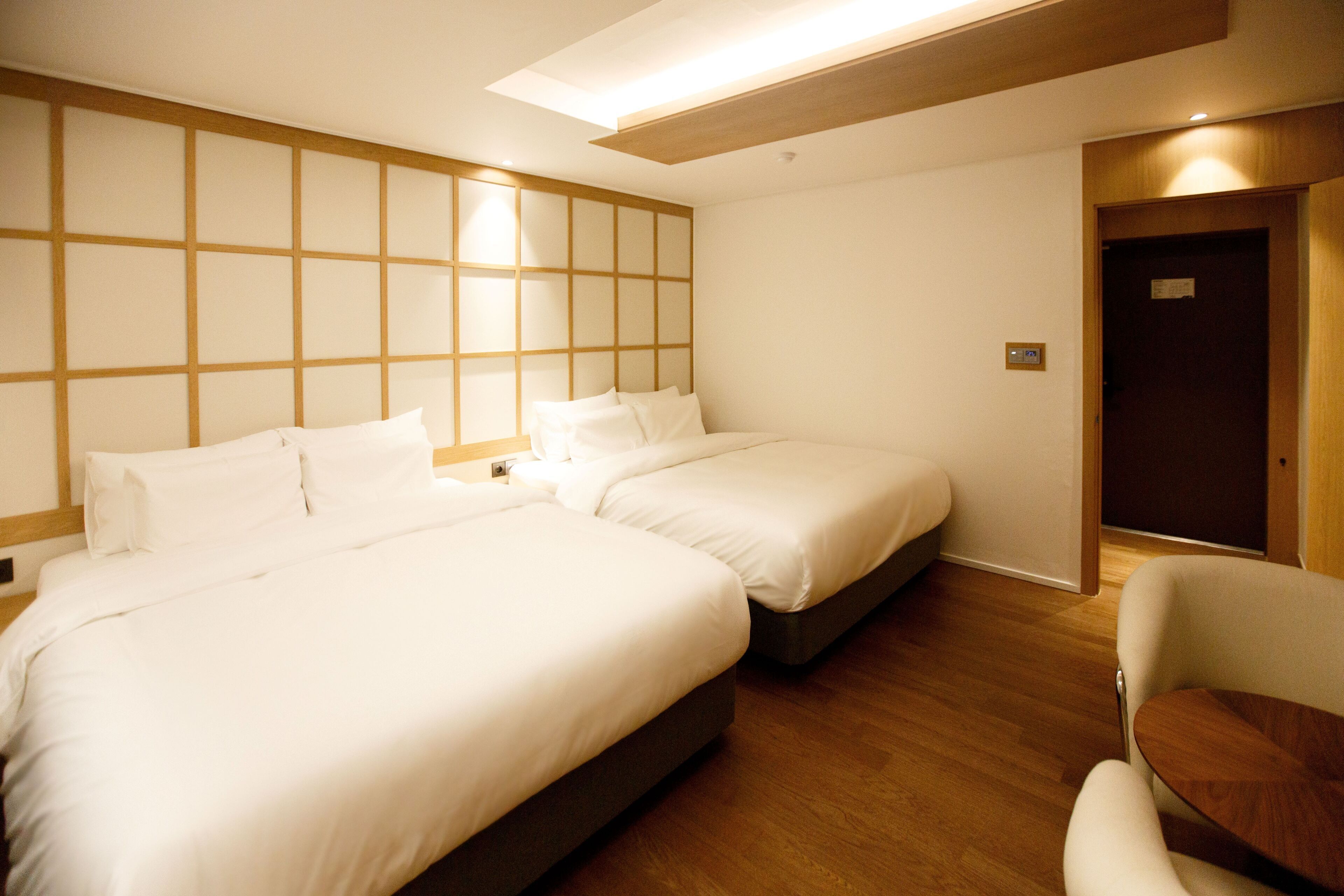 A hotel room with two beds, a wooden floor, a small table, and a door.