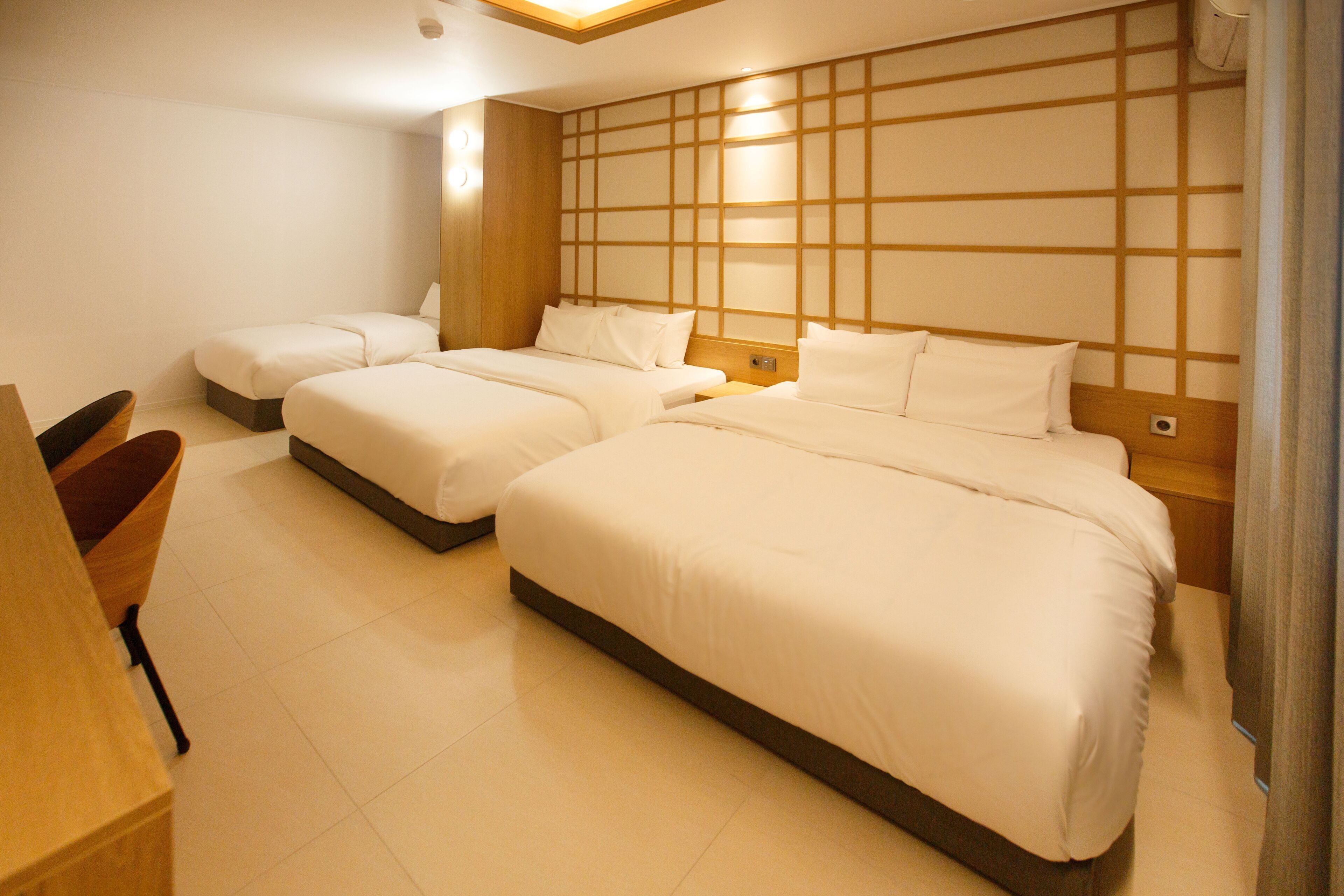 A hotel room with three beds, a wooden headboard, and a small wooden desk.