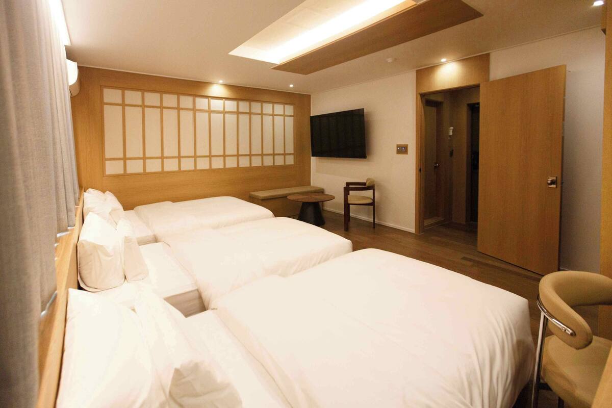 Ein Hotelzimmer mit zwei Betten, einem kleinen Tisch, einem Stuhl, einem Fernseher und einer Wand aus Holzpaneelen.