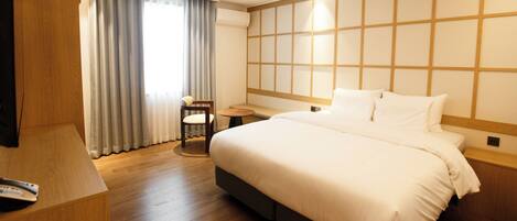 Habitación de hotel con una cama grande, un escritorio, una silla y vistas al exterior a través de la ventana.