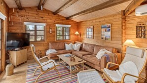 Een knus interieur van een chalet met een bank, stoelen, een salontafel en een televisie.