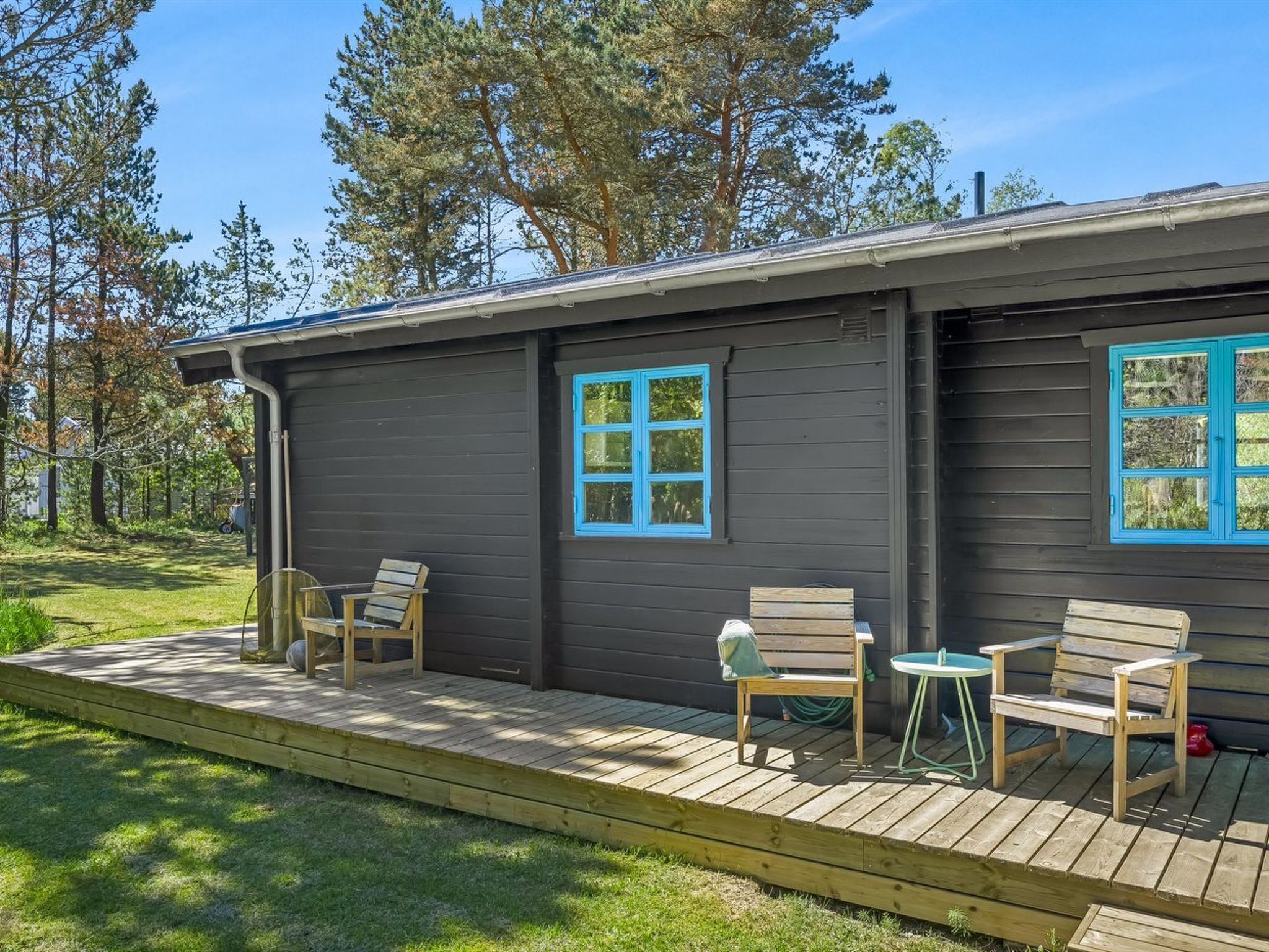 A cabin with a deck, two windows with blue trim, and a small table and chair.