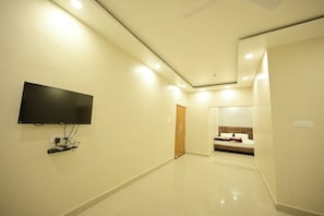 A hallway with a TV mounted on the wall, a door leading to a bedroom, and a tiled floor.