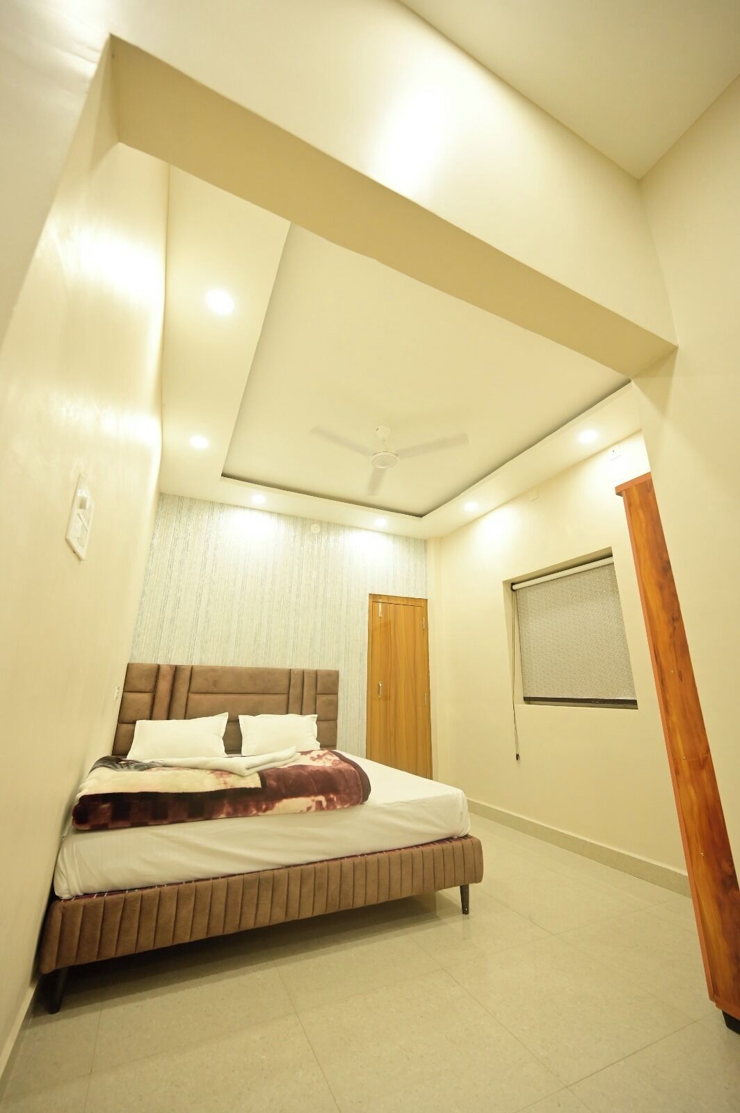 A bedroom with a bed, a ceiling fan, a wooden door, and a window with blinds.