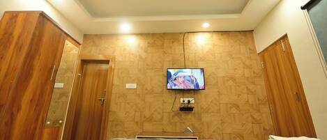 A hotel room with a bed, a television mounted on the wall, wooden paneling, and a ceiling fan.