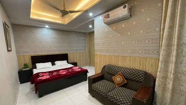 A bedroom with a bed, a sofa, a ceiling fan, an air conditioning unit, and patterned wallpaper. - The Palace Inn hotel with in peaceful Lahore (Lahore)