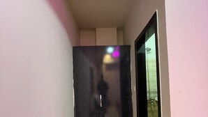 A narrow hallway with a wooden floor, a black door, and a small mat at the entrance. - The Palace Inn hotel with in peaceful Lahore (Lahore)