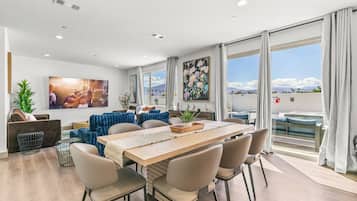 A modern living room with a dining area, large windows, and a view of the outdoors.