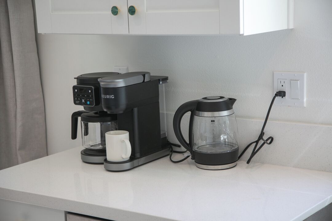 A kitchenette with a coffee maker, a glass carafe, and a white mug on a white countertop.