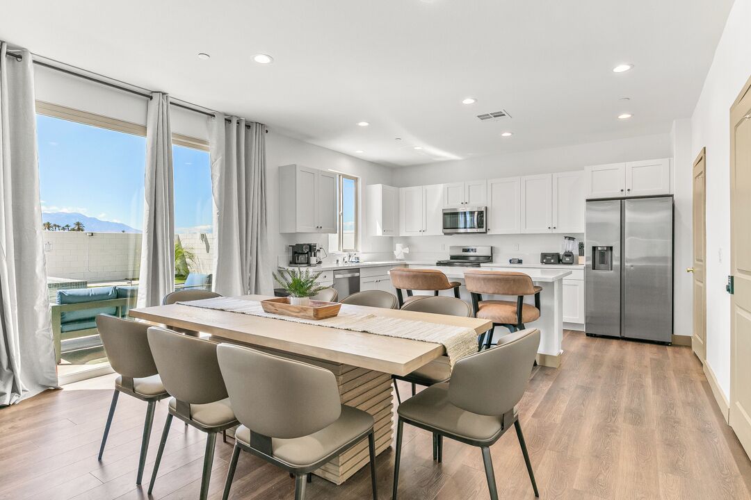 A modern kitchen with white cabinets, a stainless steel refrigerator, and a dining area with a wooden table and chairs.