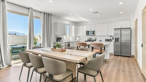 A modern kitchen with white cabinets, a stainless steel refrigerator, and a dining area with a wooden table and chairs. - 9 Bedroom/Lazy River/Sleeps 24/Pickleball/Theater (Coachella)