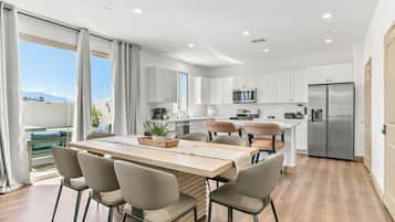 A modern kitchen with white cabinets, a stainless steel refrigerator, and a dining area with a wooden table and chairs.