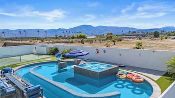 A swimming pool with a hot tub, lounge chairs, and a view of mountains.