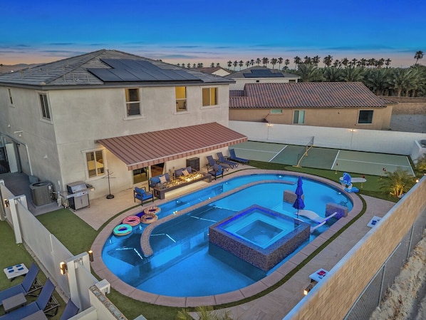 Una propiedad residencial con piscina, mobiliario exterior y cancha de tenis.