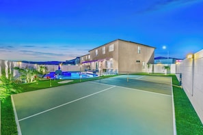 Una cancha de tenis con piscina, un edificio de techo plano y cielo despejado.