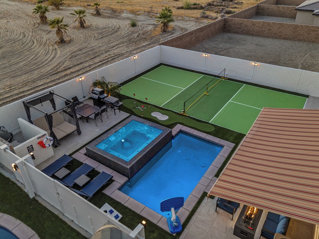 A rooftop pool with a tennis court, lounge chairs, and a hot tub.