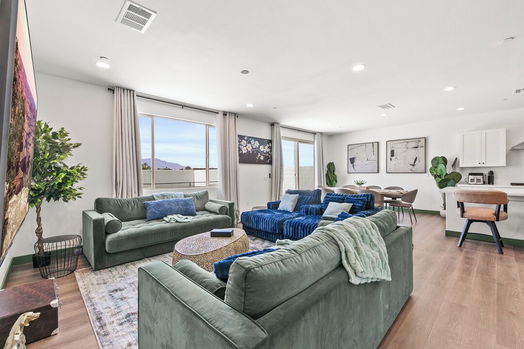 A modern living room with green sofas, a coffee table, and a dining area with a kitchen in the background.