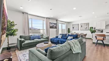 A modern living room with green sofas, a coffee table, and a dining area with a kitchen in the background.