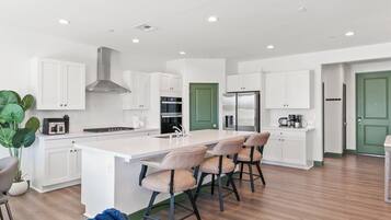 A modern kitchen with white cabinets, a central island with bar stools, a green door, and a stainless steel refrigerator.