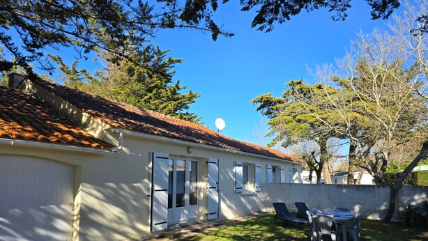 Uma casa com telhado de cerâmica, garagem e um pátio com mesa e cadeiras.