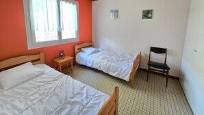 Quarto com duas camas, uma cadeira, uma mesinha e uma janela com cortinas.