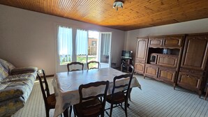 Uma área de refeições com mesa e cadeiras, um sofá, armários de madeira e uma televisão.
