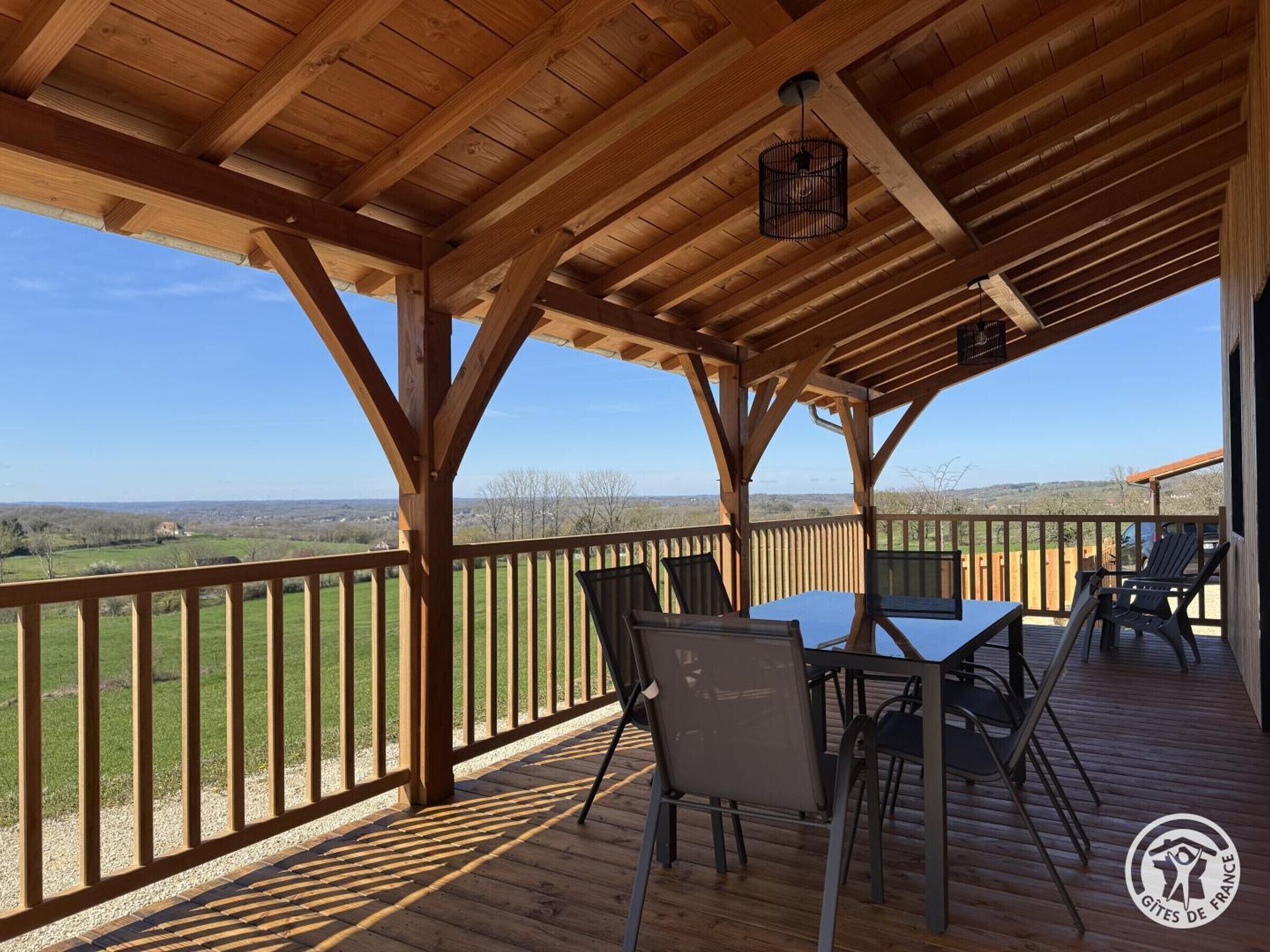 Un espacio al aire libre cubierto con una mesa y sillas, vigas de madera y vistas del paisaje.
