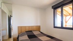 A bedroom with a wooden headboard, a checkered bedspread, and a window with a view of a wooden deck. - Single-storey house, pets allowed - 2 guests (Preyssac-d'Excideuil)