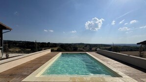 A rectangular swimming pool with a wooden deck surrounding it, set against a backdrop of a clear sky and distant landscape. - Single-storey house, pets allowed - 2 guests (Preyssac-d'Excideuil)