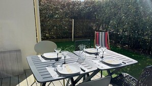 Eine Terrassengruppe im Freien mit Tisch und vier Stühlen, umgeben von einem kleinen Garten mit Zaun und Pflanzen.