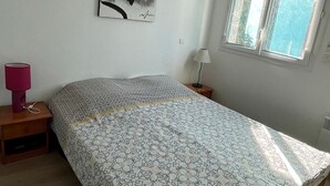Ein Schlafzimmer mit Bett, Nachttisch, Lampe, Fenster und Wandbild.