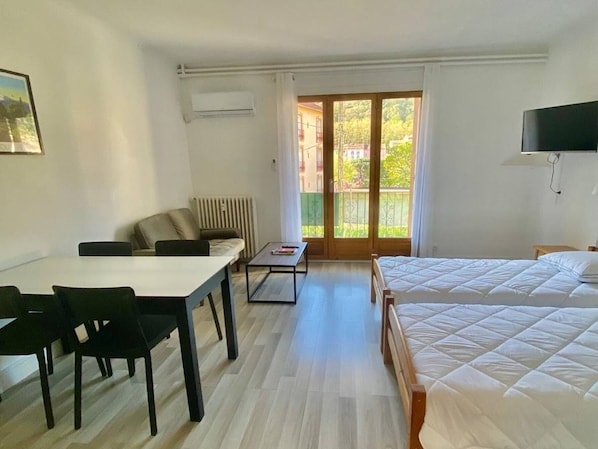 Ein Hotelzimmer mit Bett, Schreibtisch mit Stühlen, einem kleinen Tisch, einer Heizung und einem an der Wand befestigten Fernseher.