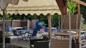 Un área de estar al aire libre con mesas y sillas, una sección cubierta y una estructura de pérgola de madera.