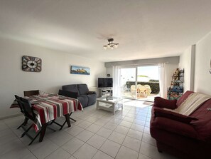 Ein Wohnzimmer mit Esstisch, Sofa, Fernseher und einem Balkon mit Gartenmöbeln.