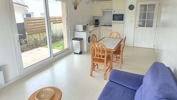 A compact living space with a dining area, kitchenette, and a sliding glass door leading to a garden. - Calm apartment with parking - 4 guests (Cucq-Stella Plage)