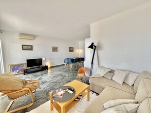 A living room with a sofa, a coffee table, a TV, a dining table with chairs, and a floor lamp. - Apartment with AC, sea view - 4 guests (Ajaccio)