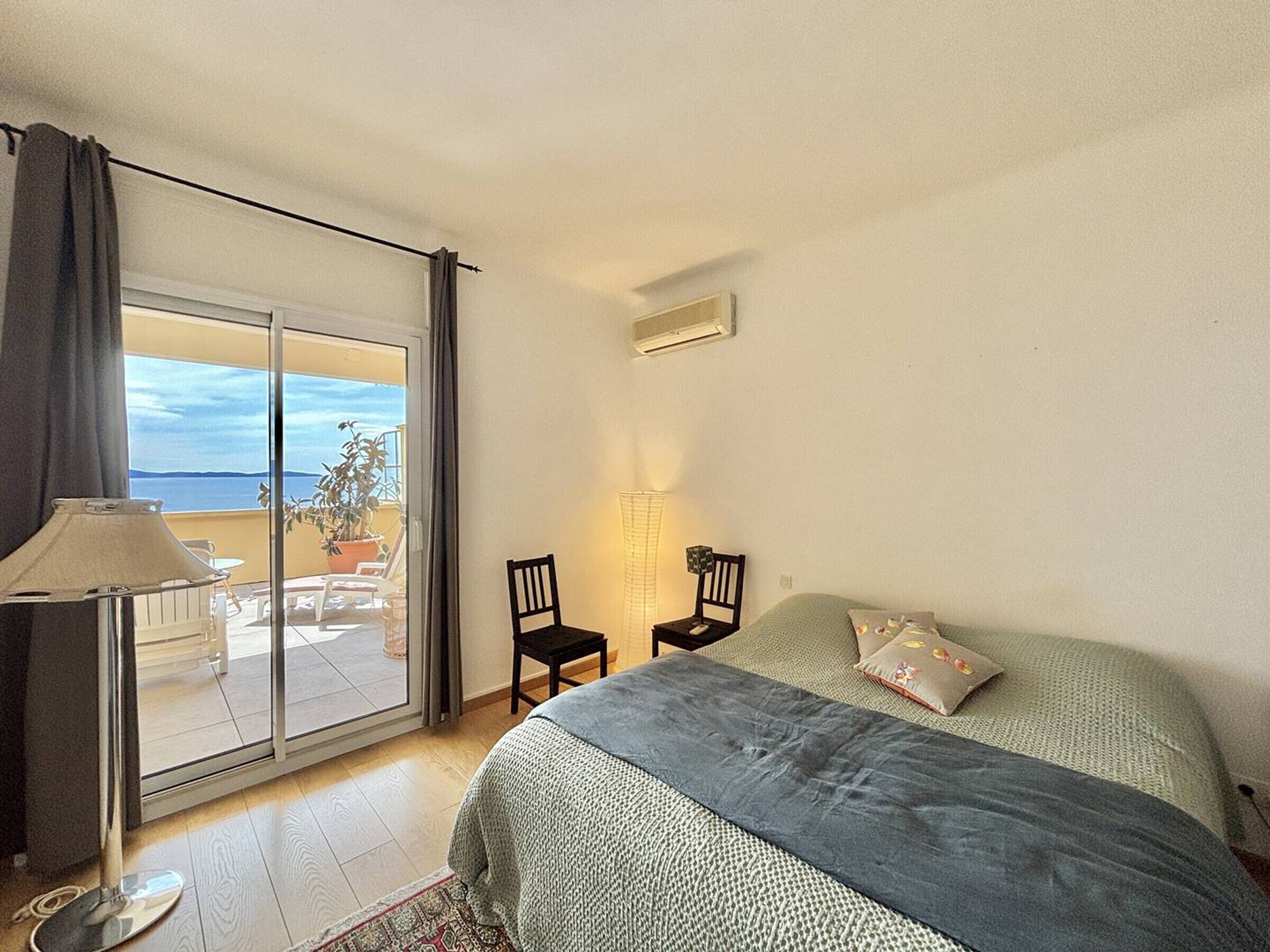 Un dormitorio con cama, una silla, una lámpara y vista al mar a través de una puerta corrediza.