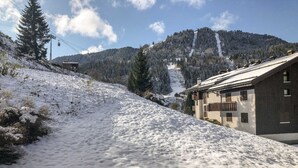Pendio innevato con un edificio sulla destra, una seggiovia sullo sfondo e una montagna boscosa.