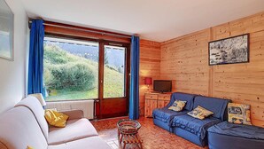 Un soggiorno accogliente con un divano, una poltrona, una televisione e vista sul verde.