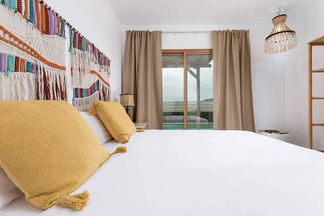 A bedroom with a bed, curtains, a chandelier, and a view through a window.